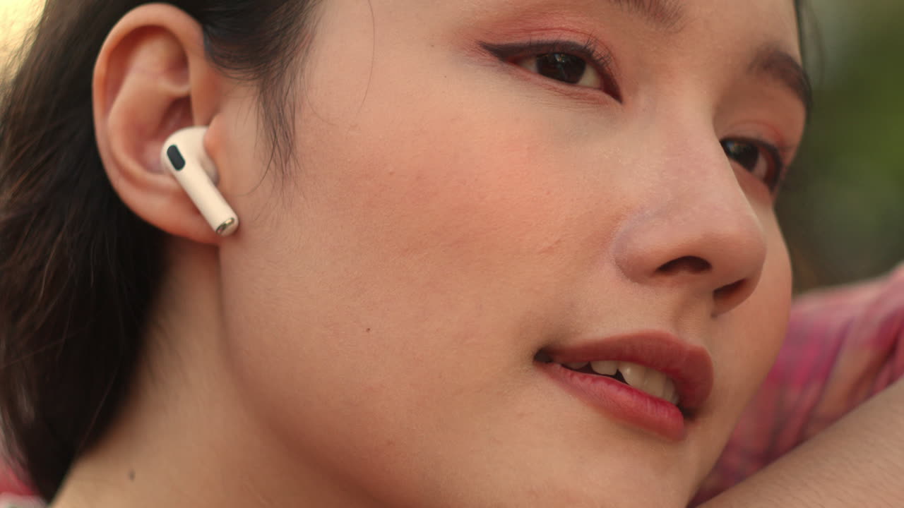 ritratto di una modella femminile asiatica che ascolta musica con gli auricolari durante il caldo estivo raffreddando la temperatura usando un ventilatore microelettrónico