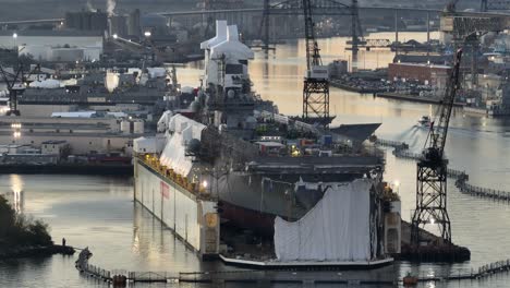 warship in dry dock at a naval shipyard during sunrise