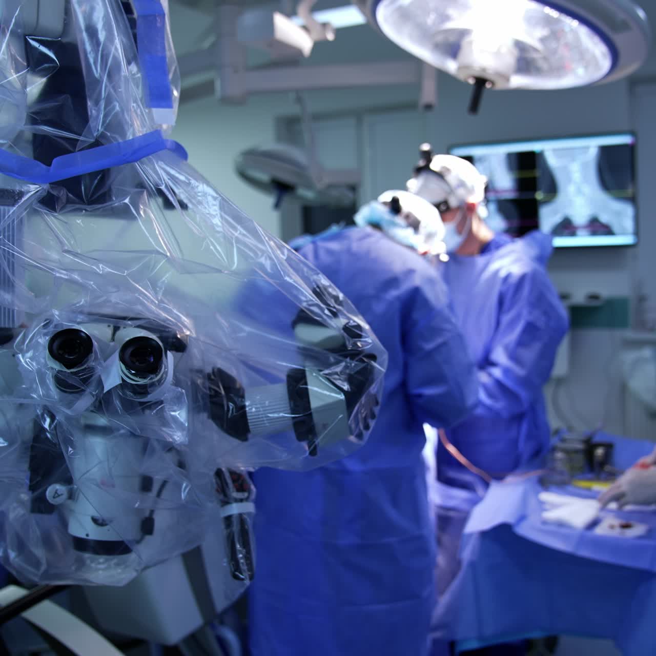 Advanced microscope coated with plastic in surgery room. Surgical team working at operational table at backdrop