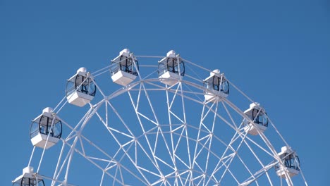 4k. close-up of a white ferris wheel slowly rotating against the blue sky on a sunny day.