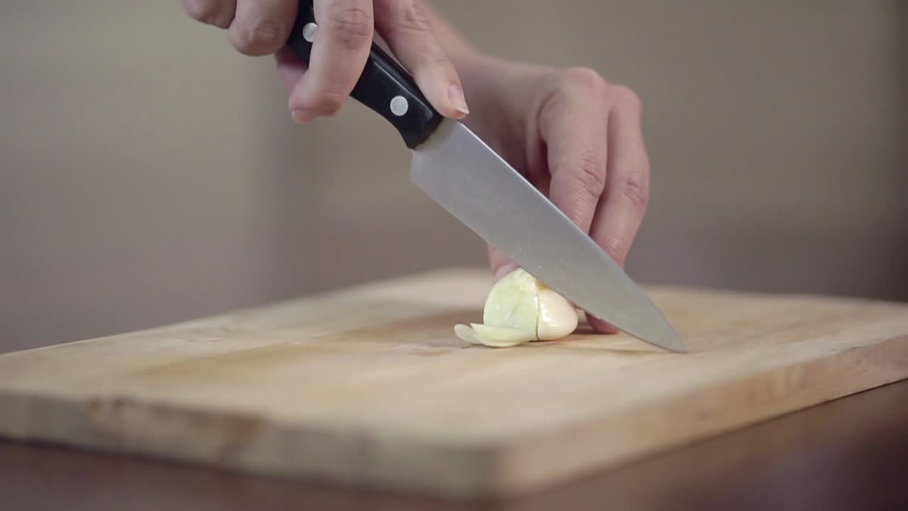 Primo piano di mani che tagliano aglio fresco su un tagliere di legno
