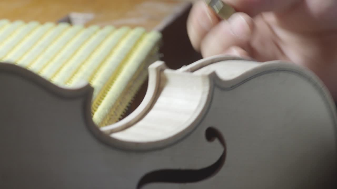 macro primer plano de artesano luthier fabricante de trabajo en nuevo clásico hecho a mano violín crudo borde liso en la cintura y raspado púrpura en el banco de trabajo del taller en cremona italia video 4k