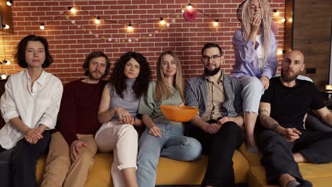 retrato de amigos viendo un programa de comedia en la televisión y comiendo palomitas de maíz mientras están sentados en un sofá en casa