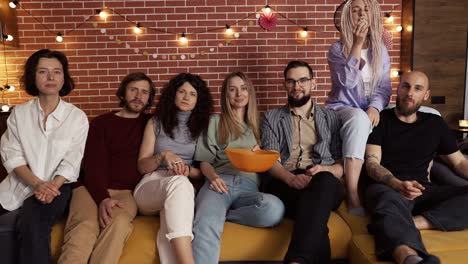 portrait of friends watch comedy show on tv and eat popcorn while sitting on a sofa at home