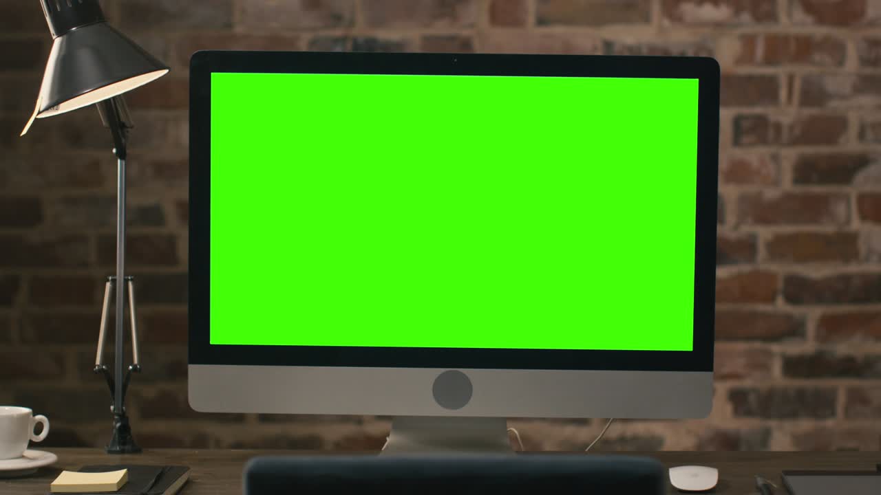 초록색 화면으로 된 컴퓨터 모니터가 테이블에 서 있고, 에 태블릿, 램프, 커피 컵, 노트북, 마우스가 있습니다.