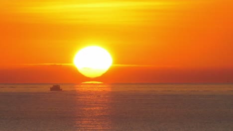 Fishing-boat-silhouette-against-orange-sunrise-over-calm-sea,-sun-on-horizon