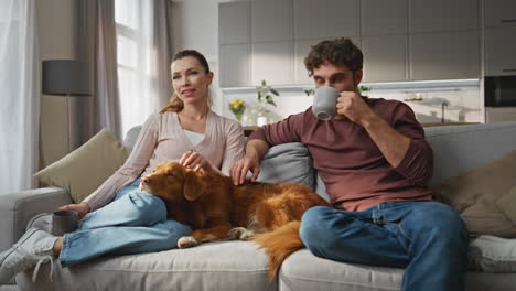 relaxed spouses chilling home couch caressing dog. couple sitting on cozy sofa