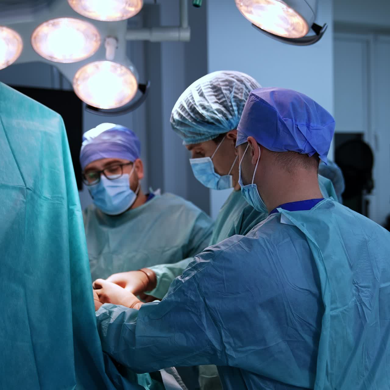 Three doctors operating the patient in modern surgical room. Team of surgeons cooperating at medical procedure