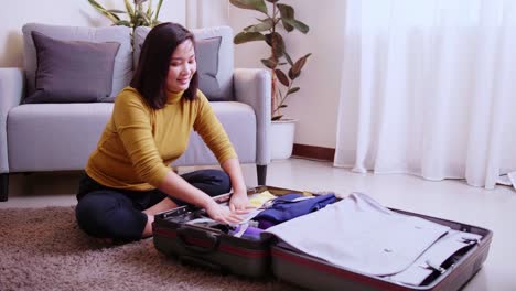 Asian-woman-arranging-clothes-in-takeout-suitcase-in-her-living-room