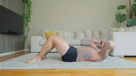 shirtless man with tattoo doing sit-ups and crunches exercising abdominal muscles