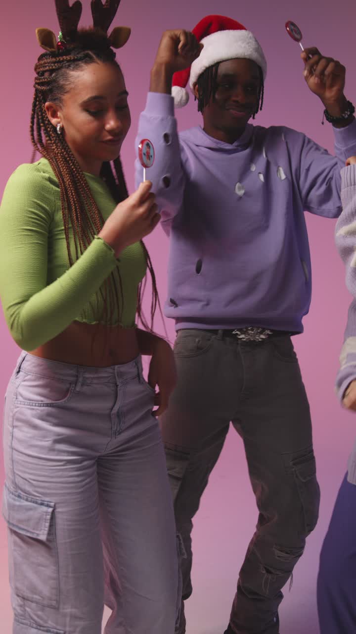 Vertical Video Studio Shot Of Gen Z Friends Dancing At Christmas Party Wearing Santa Hat And Reindeer Antlers 1