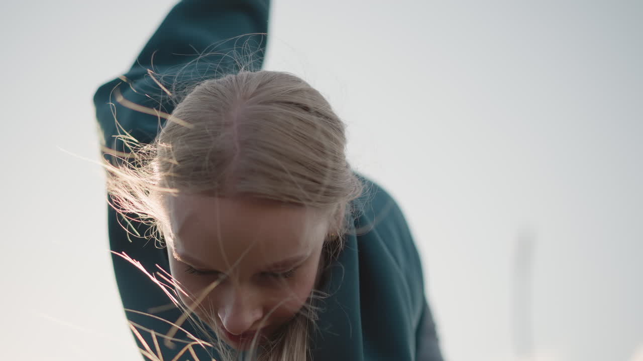 primer plano de una joven con un suéter verde inclinándose hacia adelante durante el entrenamiento con el cabello revoloteando en el viento, mostrando determinación y movimiento contra un fondo de cielo brillante