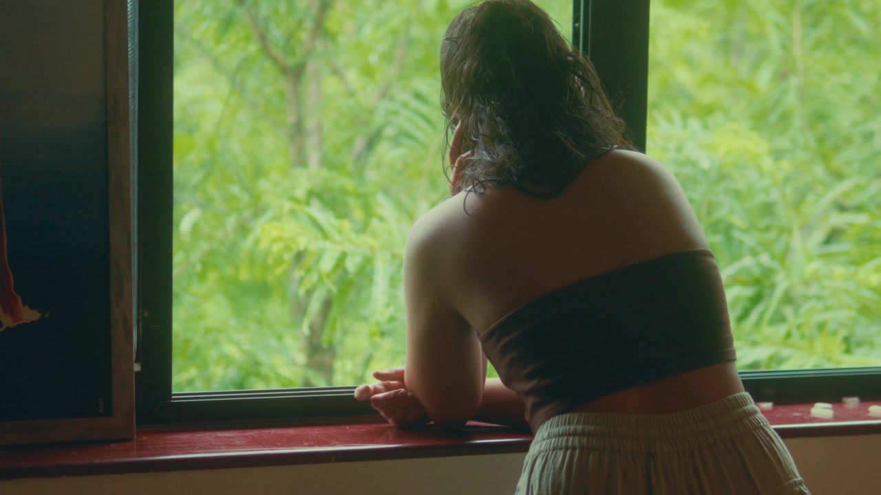 Woman leans on window ledge then straightens while looking outside