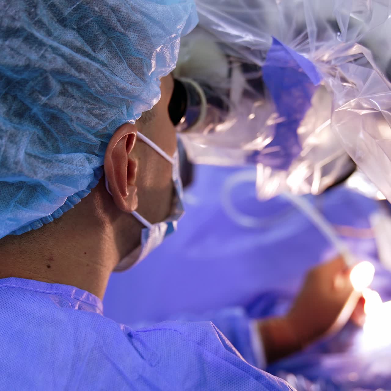 Rear view of a male doctor's head in cap and mask turned to the microscope. Neurosurgeon performs operation in modern clinics