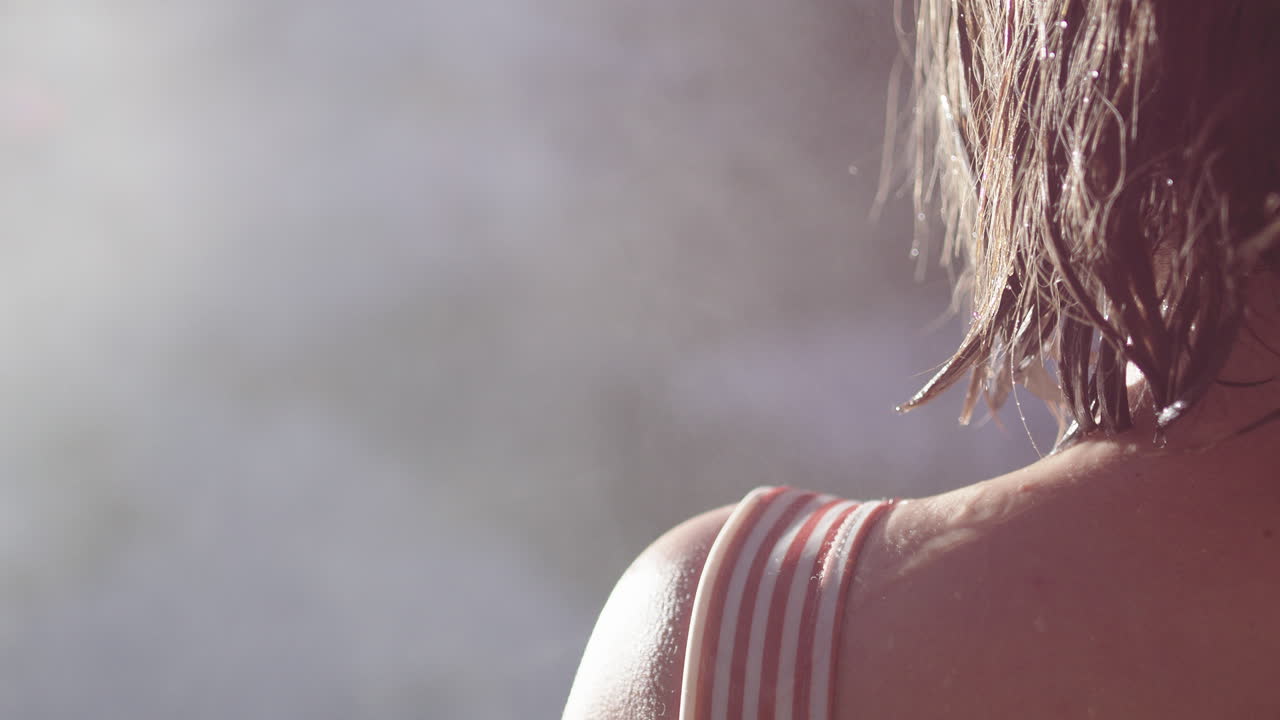 Woman steps out of steaming hot sauna into brisk winter air, over shoulder shot