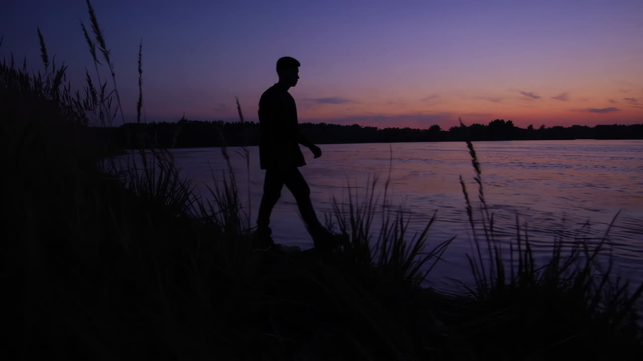 Silhouette of person walking along river at sunset