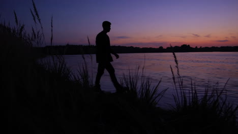 silhouette of person walking along river at sunset