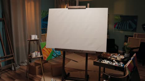 a workspace, a studio of a painter, an artist with a large easel with a canvas in the middle of the room. around the canvas scattered paints, brushes, cardboard boxes, a mess