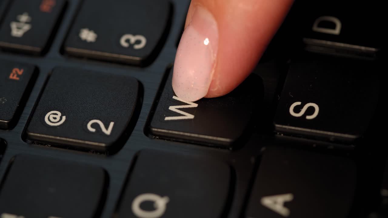 Black keyboard and a girl pushes W button. English letters. Slow-mo and girl has a pink nail polish.