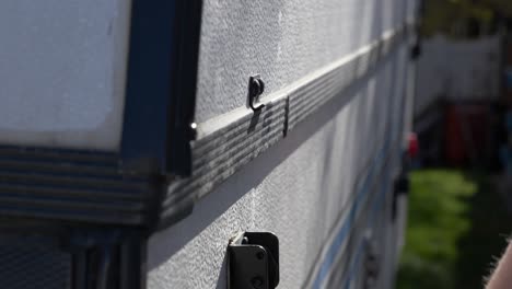 a hand removes a clasp on a tent trailer getting ready to set it up and go camping