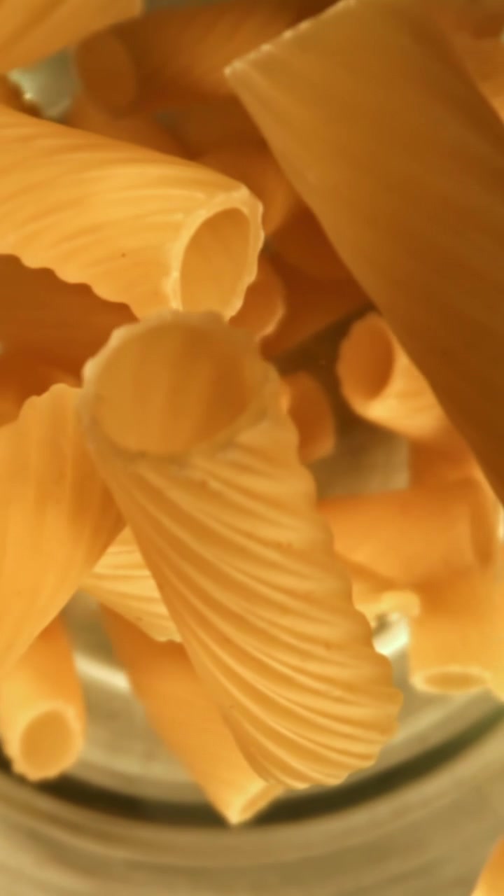 Rigatoni dorati che cadono in un contenitore al rallentatore
