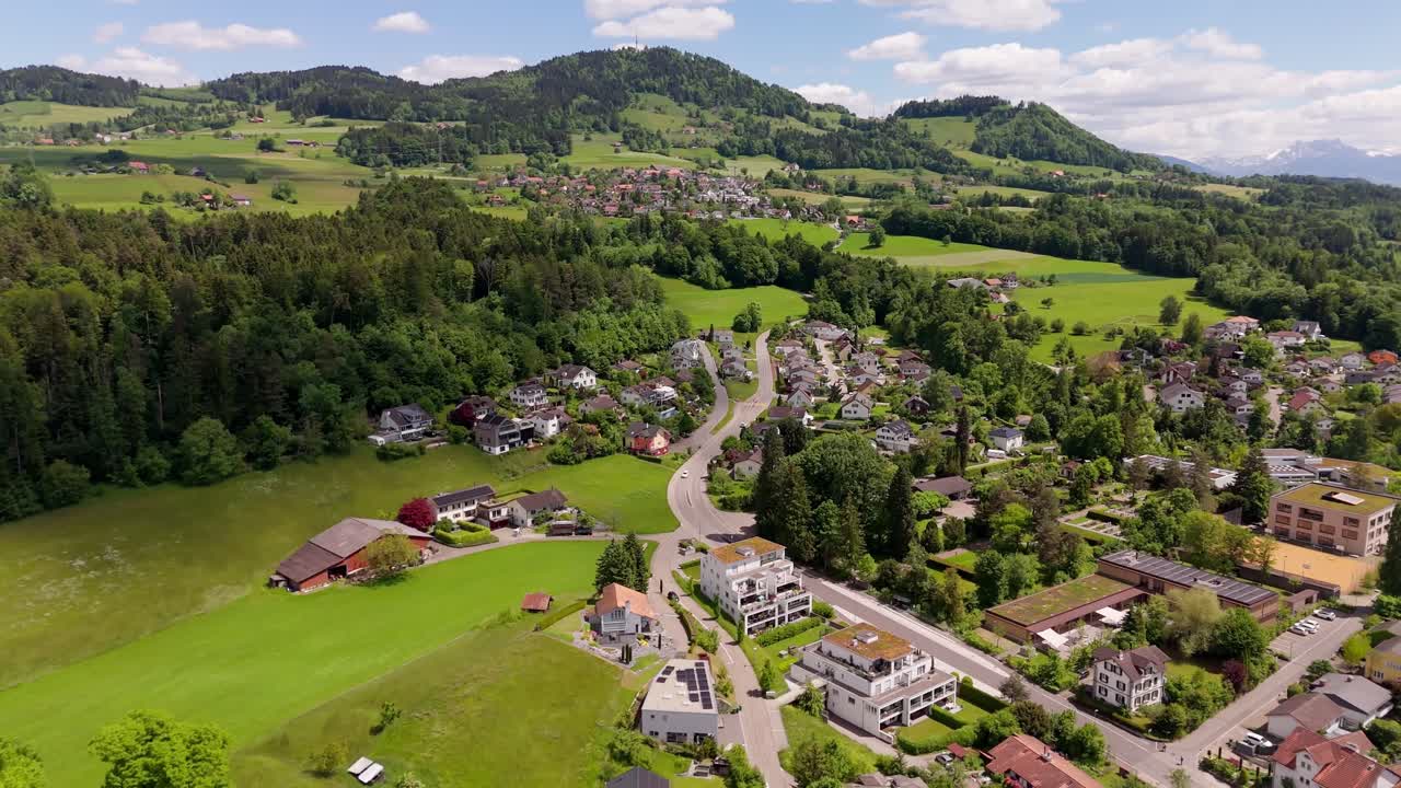 Drone flight over swiss city of Hinwill with luxury apartment houses in idyllic mountains of Switzerland. Aerial forward wide shot. Green forest landscape and hills in distance. Modern buildings.