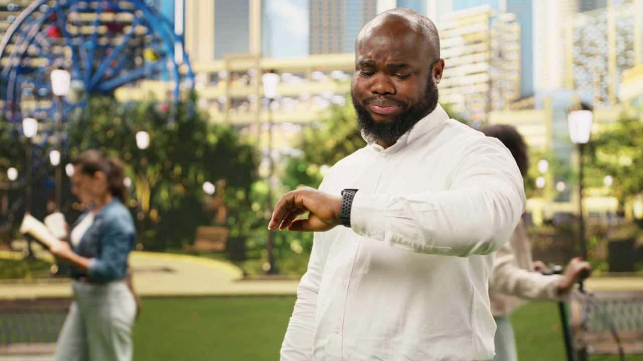 Concerned businessman checking time on smartwatch while standing in city park