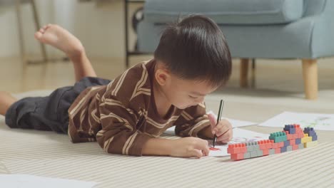 close up of asian kid lying on the floor in the room with plastic toy brick drawing at home