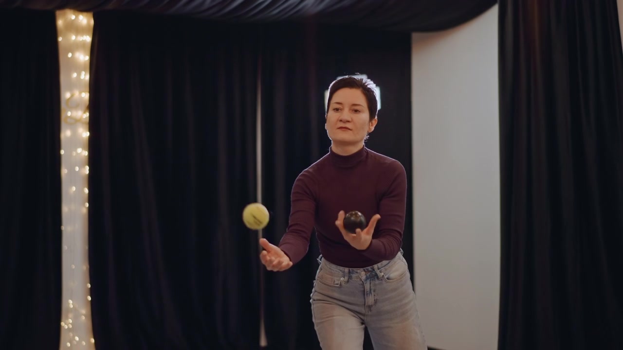 Studio solo rhythm drill with ball, performer practicing toss timing and expression, camera light and string curtain backdrop visible, energetic movement and reel friendly vibe, content creation tone