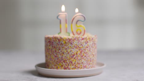 studio shot birthday cake covered with decorations and candle celebrating sixteenth birthday being blown out