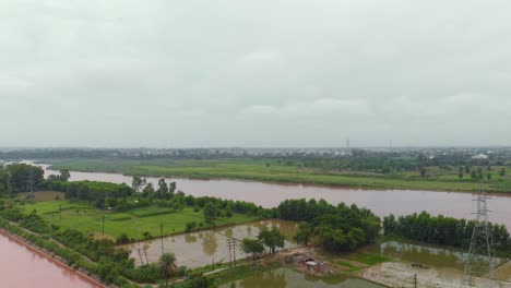 Vista-Aérea-Del-Paso-Elevado-Sobre-Tierras-Agrícolas-Cerca-Del-Río,-Y-El-Canal-Después-De-La-Lluvia-Con-Agua-Turbia-Lluviosa-Fuera-De-La-Ciudad-En-La-Región-De-Punjab,-India