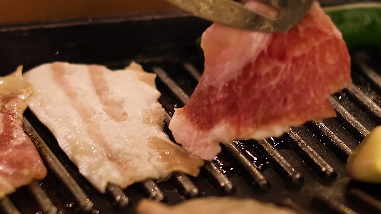 Close-up of pork slices being grilled alongside green peppers and garlic cloves on a stovetop grill.
