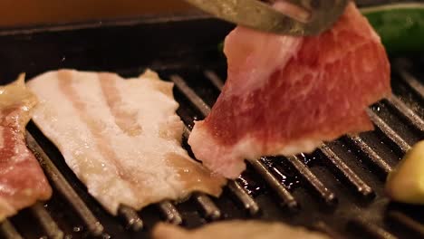 close-up of pork slices being grilled alongside green peppers and garlic cloves on a stovetop grill.
