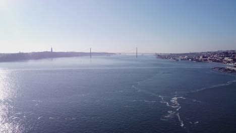 Ponte-25-De-Abril-Aus-Der-Ferne-Gefilmt-Von-Einer-Drohne-In-Großer-Höhe-über-Dem-Tejo,-Während-Sie-An-Einem-Hellen-Und-Sonnigen-Tag-Seitwärts-über-Land-Nach-Lissabon-Portugal-Fliegt