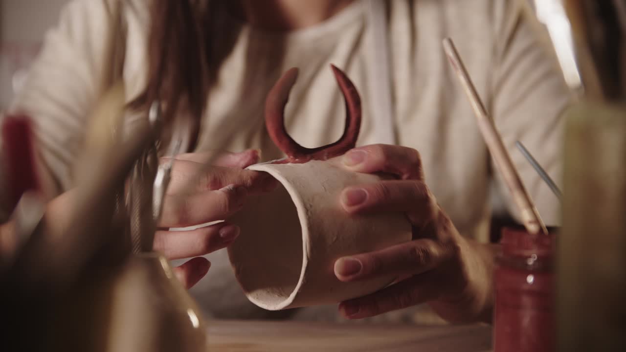joven alfarera chequeando la cubierta del diseño en una taza de cerámica con sus dedos