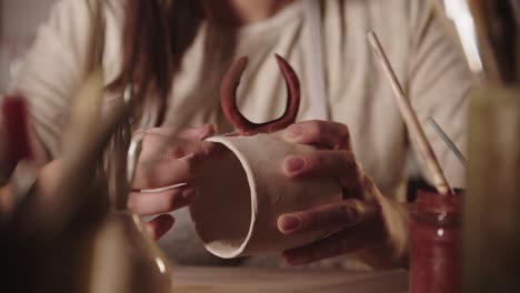 young woman potter checking the covering of design on ceramic mug with her fingers