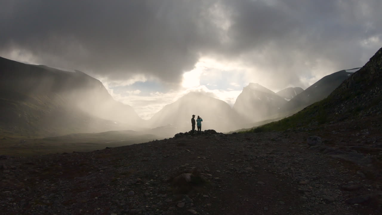 Two hikers enjoying the beautiful view over the big mountain Kebnekaise at sunset.
