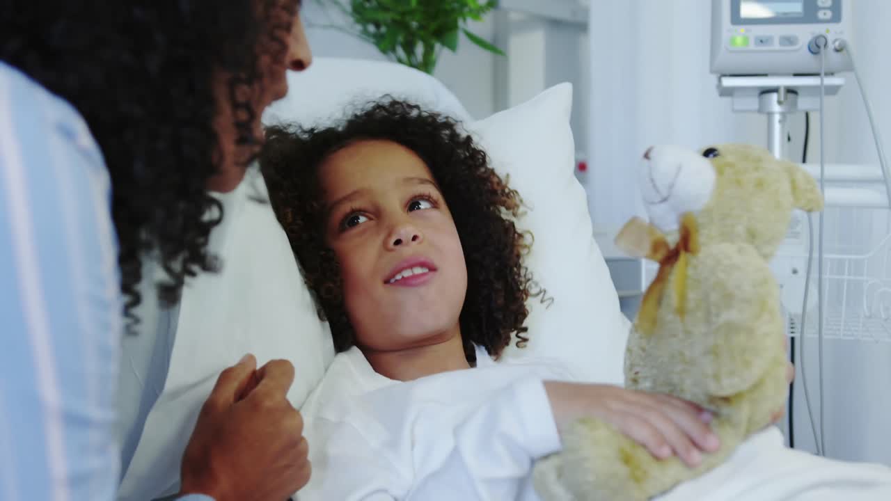 Close-up of African american mother and son playing with teddy bear in the ward at hospital 4k