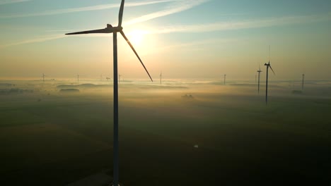 a beautiful shot of a picturesque landscape shrouded in mist at dawn, with the spinning propellers of wind turbines towering above