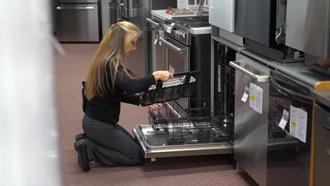 pretty mature blonde woman looking at dishwashers in a kitchen appliance store