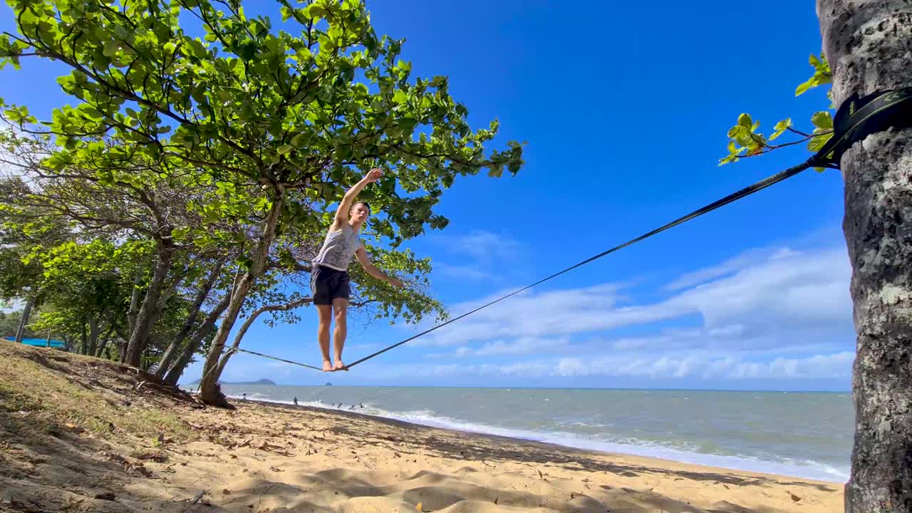 macho adulto joven caminando lentamente a lo largo de slackline en trinity beach en cairns