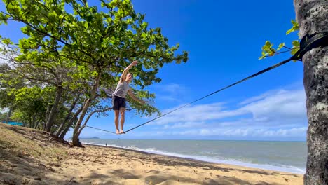 young adult male slowly walking along slackline on trinity beach in cairns