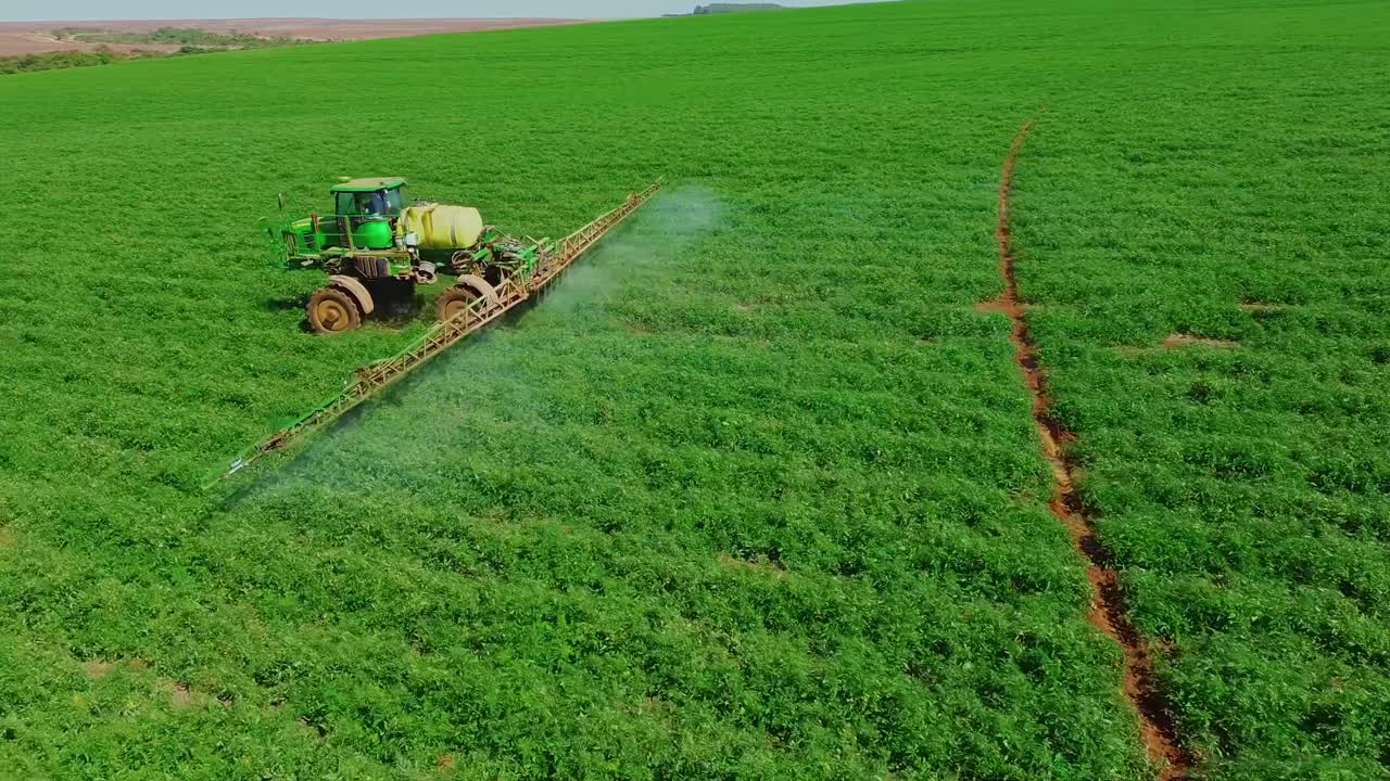 Vista aerea di un trattore che irrora le colture in un campo agricolo verde.