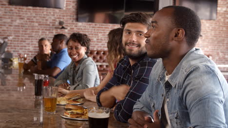 Group-Of-Friends-Watching-Game-In-Sports-Bar-On-Screens