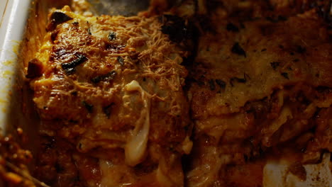 cutting and serving a portion of a delicious meat lasagne with grated cheese