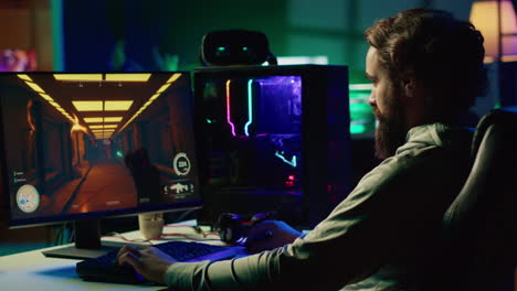 Portrait-of-smiling-man-in-dimly-lit-apartment-playing-video-games-on-gaming-PC