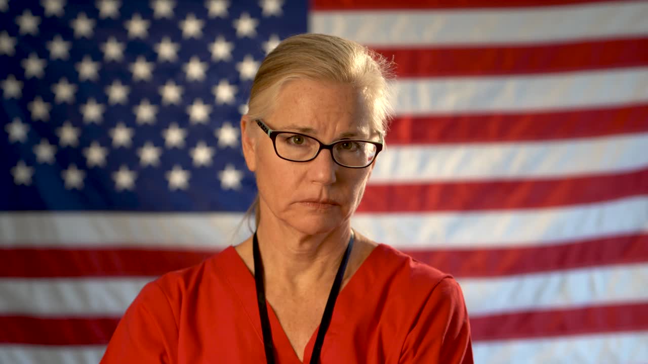 초점이 맞지 않는 미국 국기에 대해 걱정하고 공감하는 의료 간호사의 중간 꽉 초상화