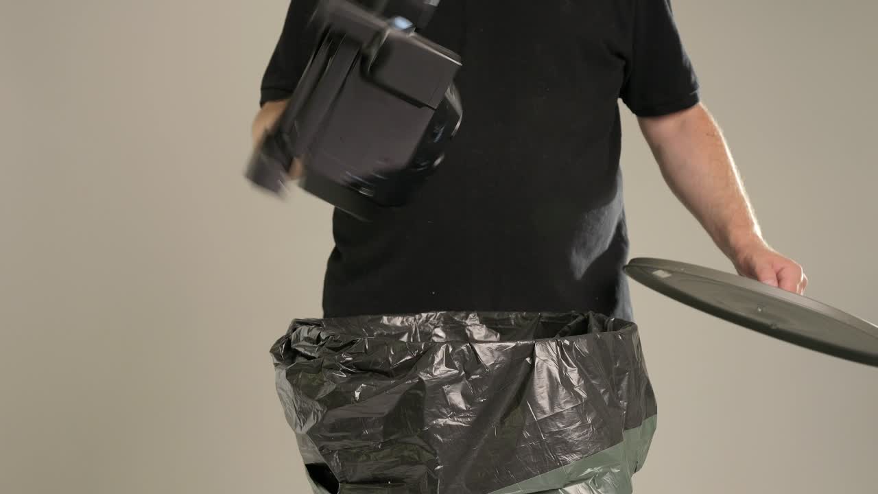 한 남자가 아주 오래된 카메라를 쓰레기통에 던지고 있다.