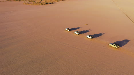 drone shot tracking a queue of 4x4 vehicles, driving across distant desert in sunny saudi arabia