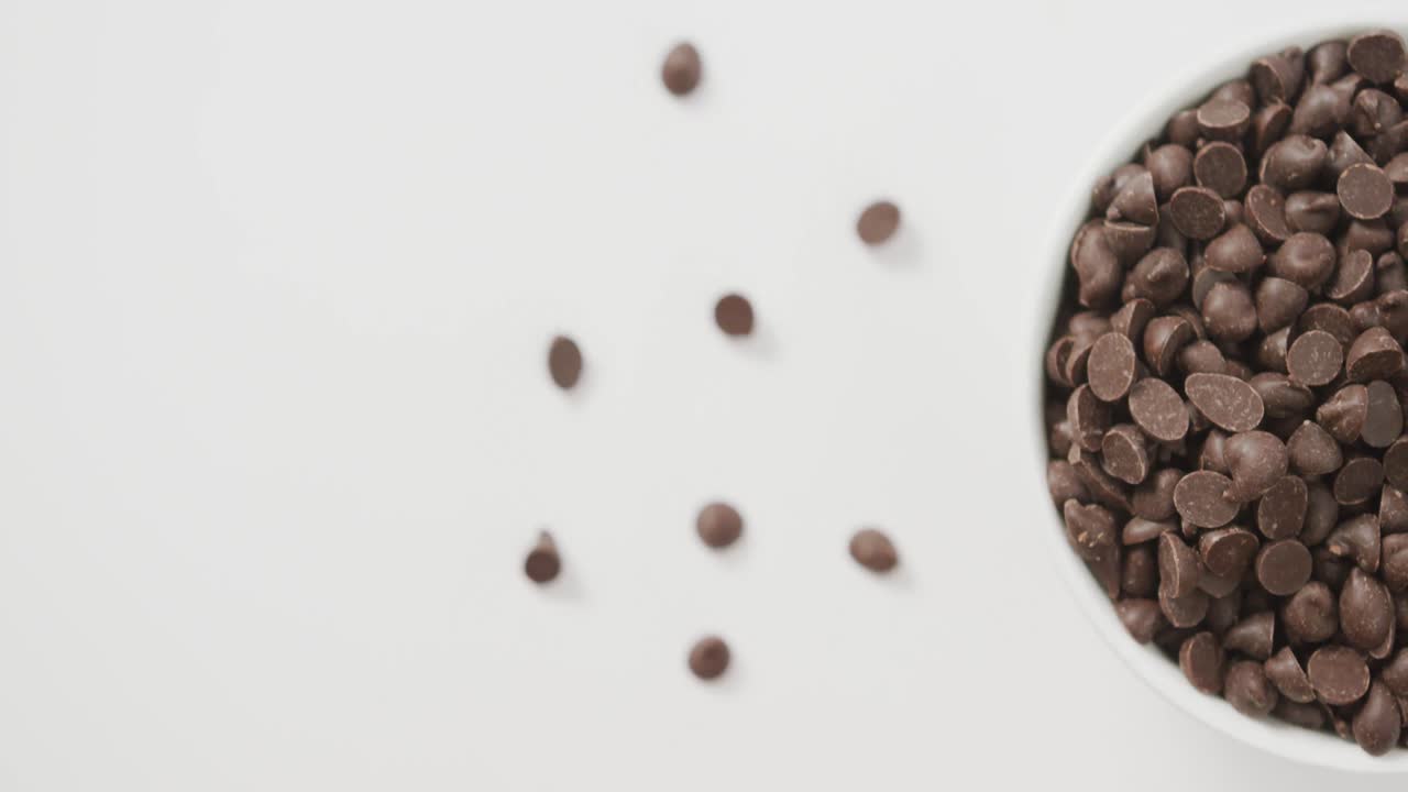 Video con vista dall'alto di una ciotola di gocce di cioccolato su sfondo bianco.